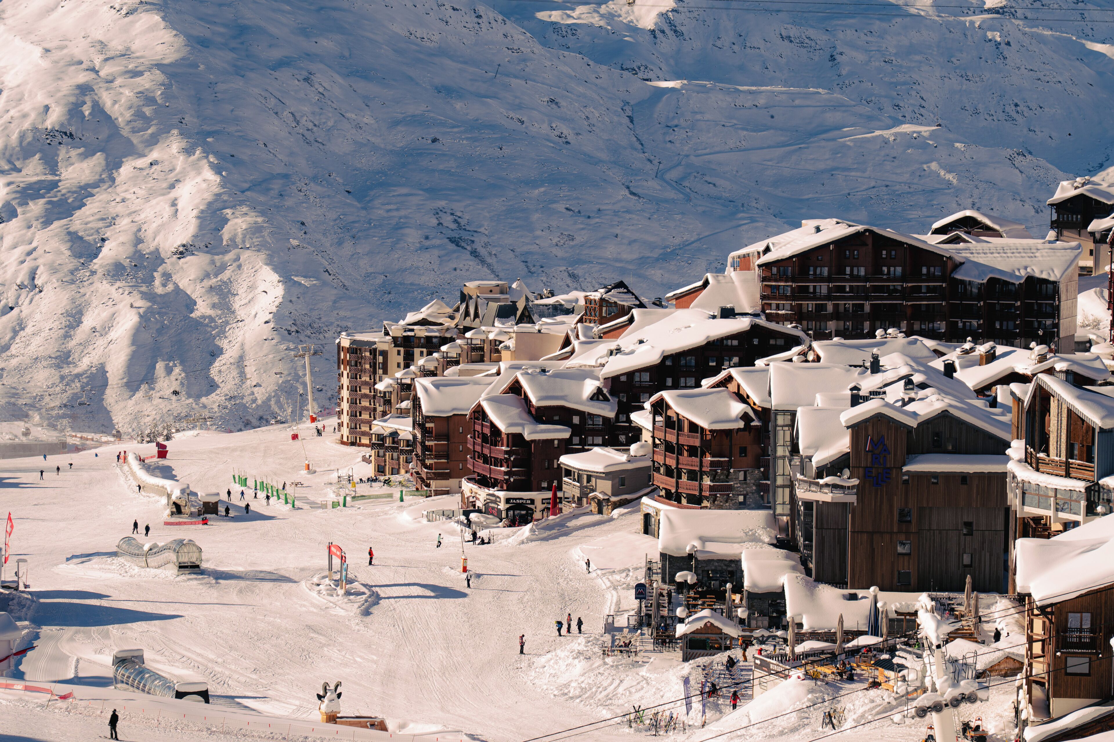 Une station de ski enneigée, avec des chalets en bois, des pistes de ski et un paysage montagneux en toile de fond.
