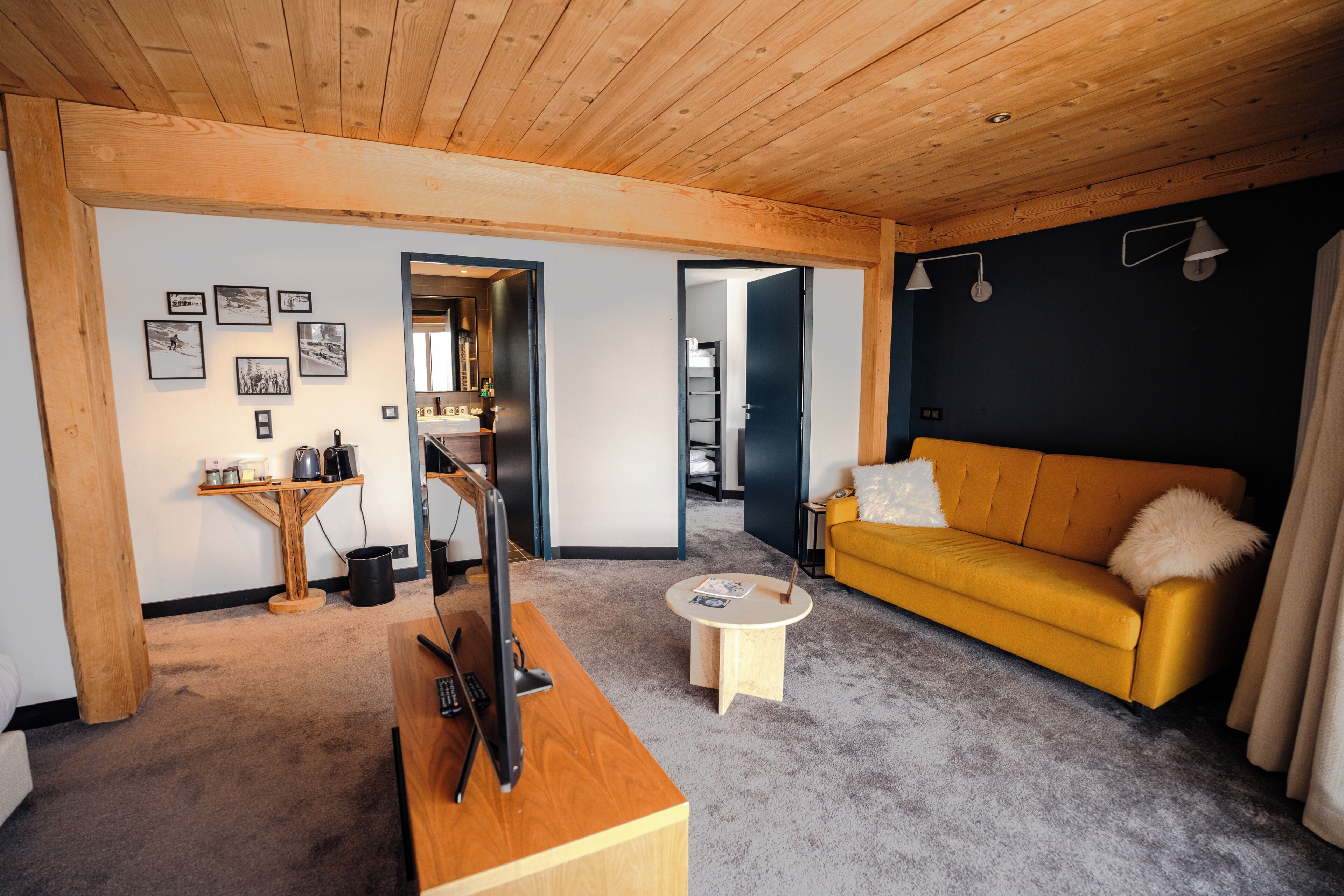Ein modernes Wohnzimmer mit Holzboden, einem gelben Sofa, einem Couchtisch und einem Fernseher auf einem Holzbodenständer.