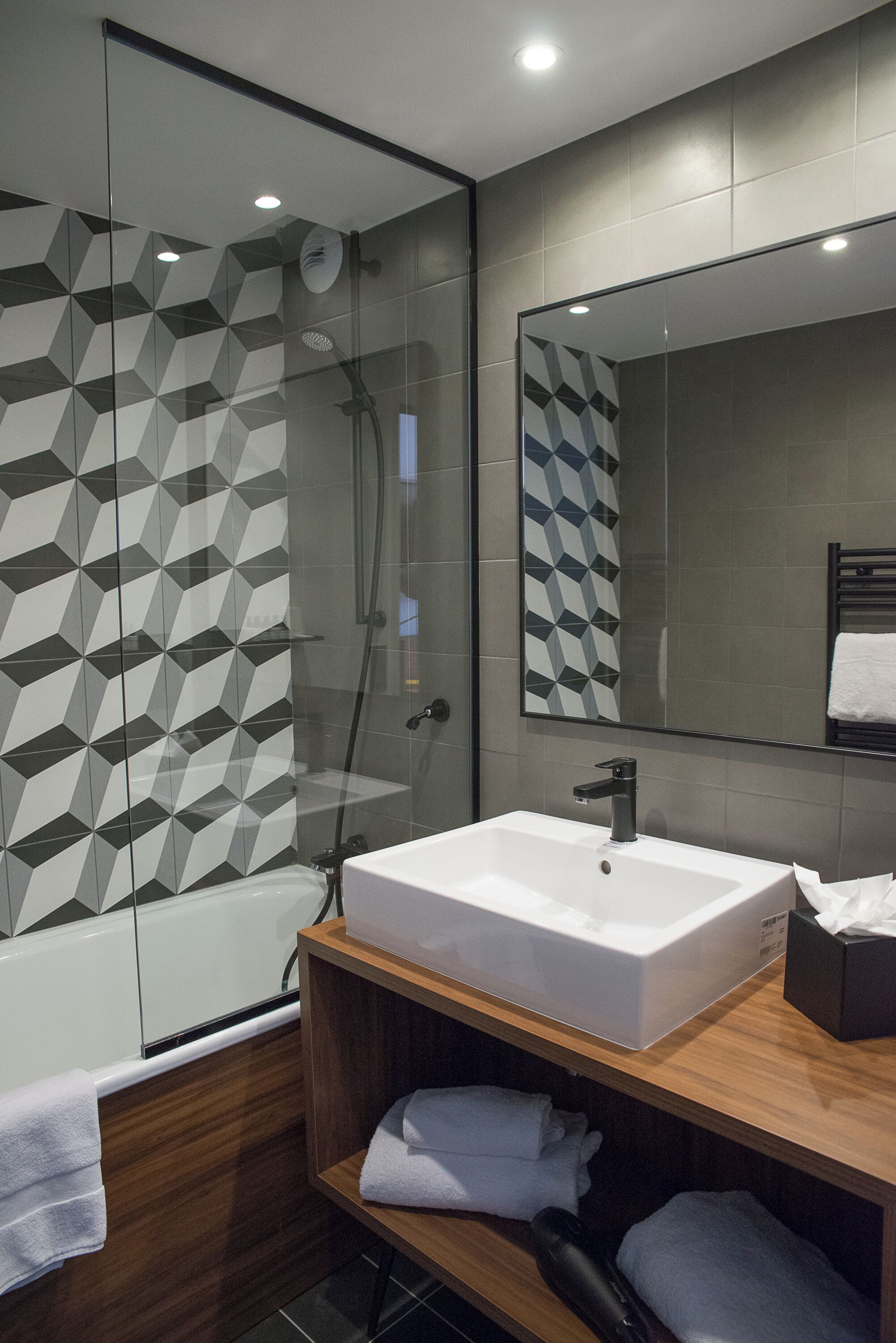 A modern bathroom with a glass-enclosed shower, a white sink, and a wooden vanity.