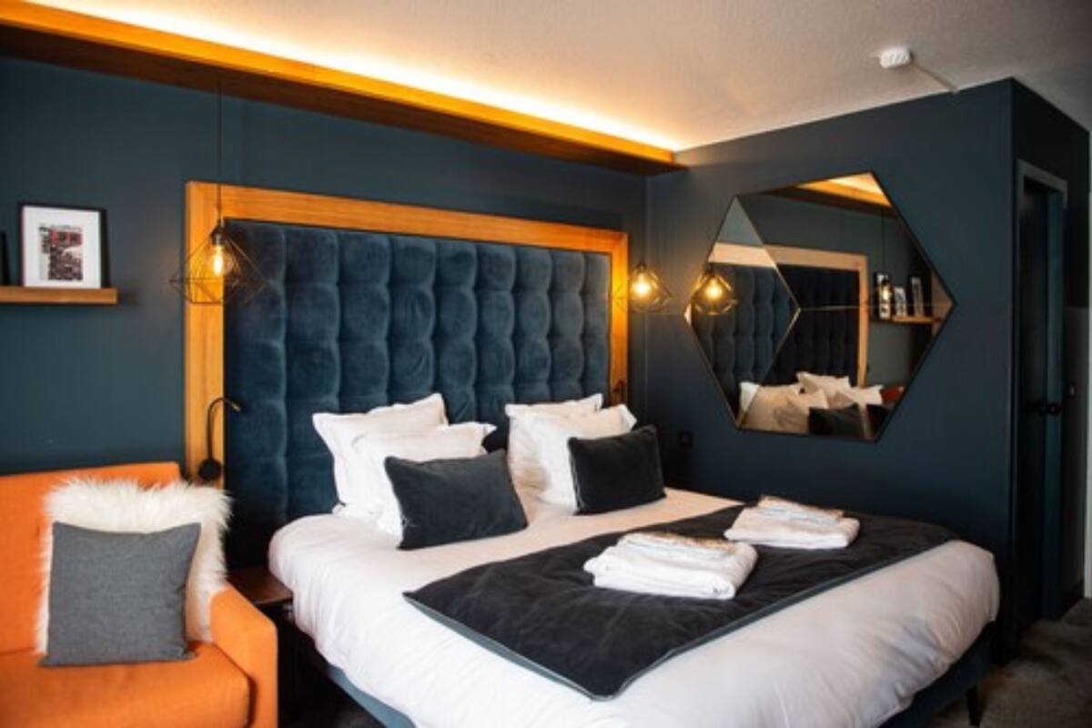 Ein modernes Hotelzimmer mit einem großen Bett, einem hölzernen Kopfteil, einem Spiegel und einem kleinen orangefarbenen Sessel.