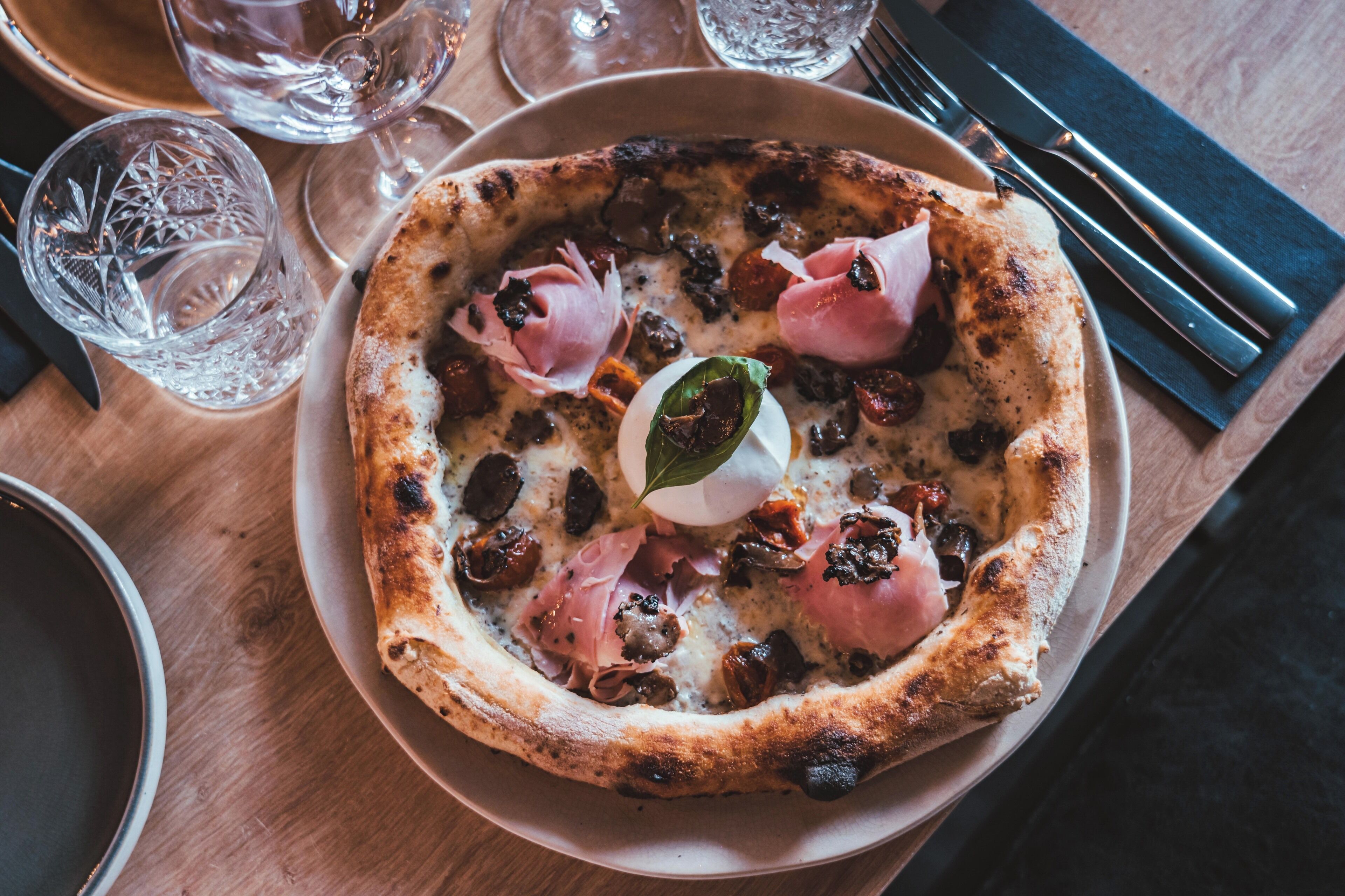 Una pizza en un plato sobre una mesa de madera, con vasos y cubiertos.