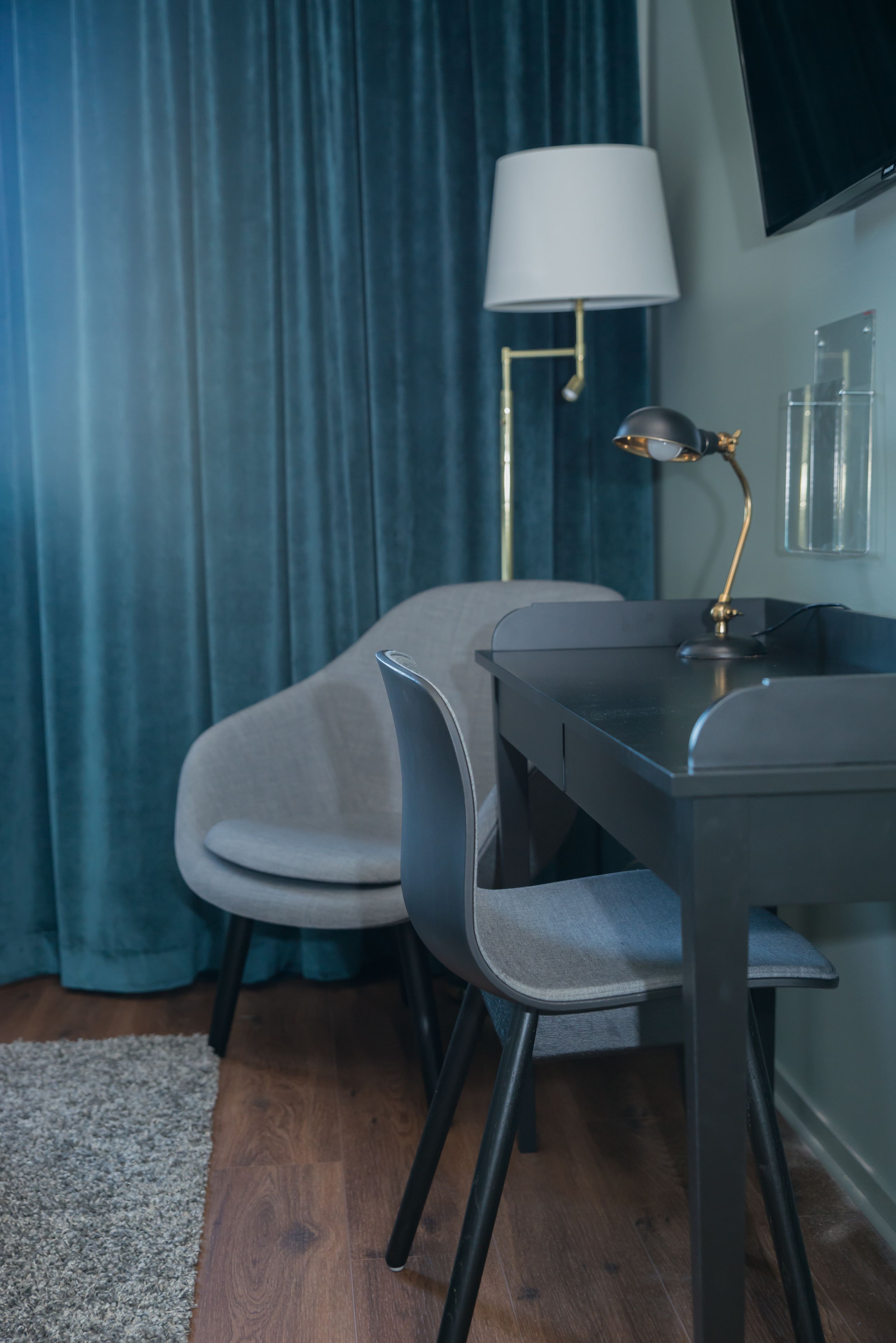 Una habitación moderna con un escritorio oscuro, dos sillas grises, una lámpara blanca y una cortina azul.