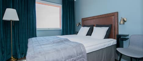 Una cama bien hecha con edredón gris, cabecera de madera y lámpara de noche.