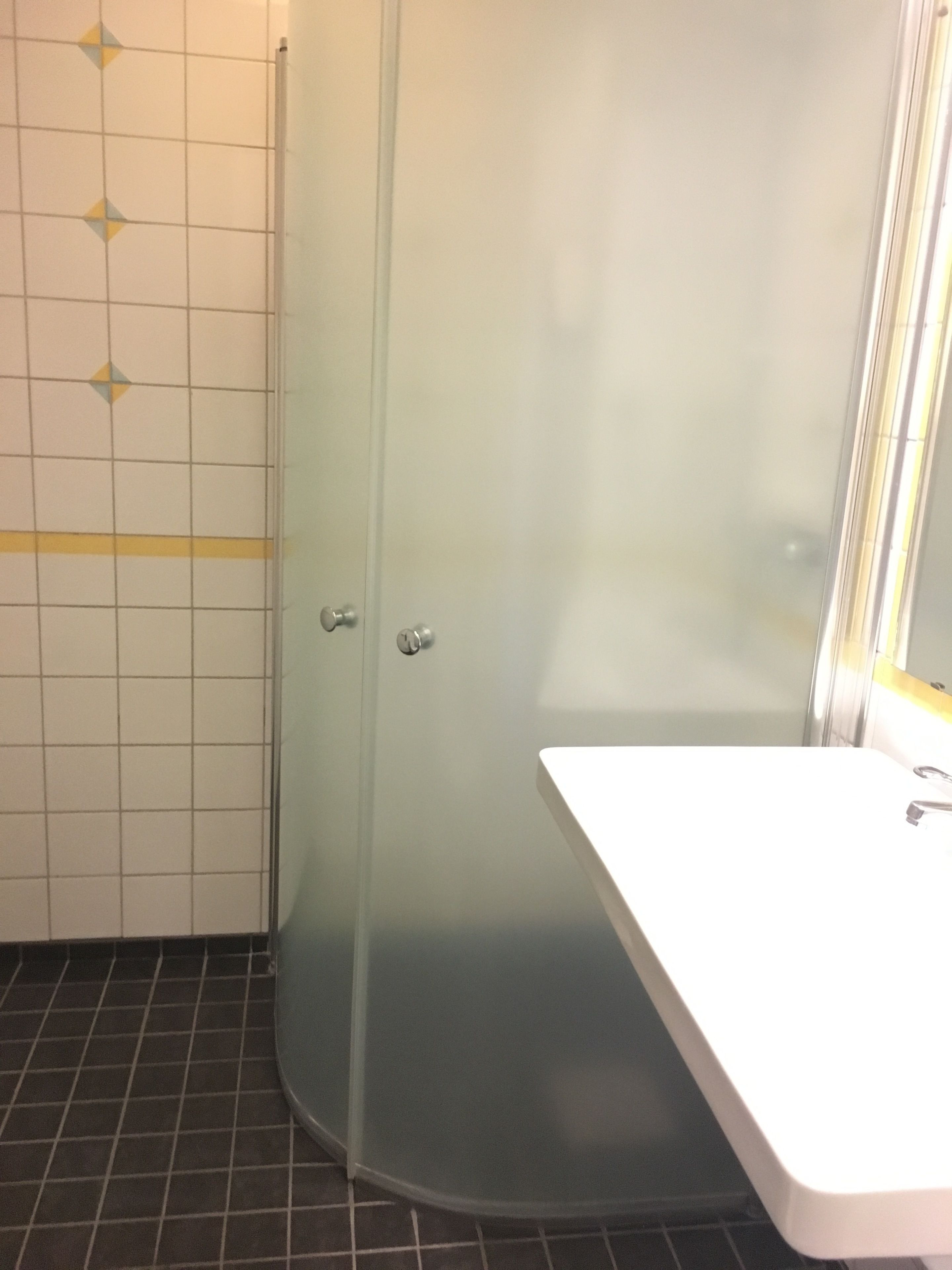 A bathroom with a glass shower enclosure, a white sink, and a tiled floor.