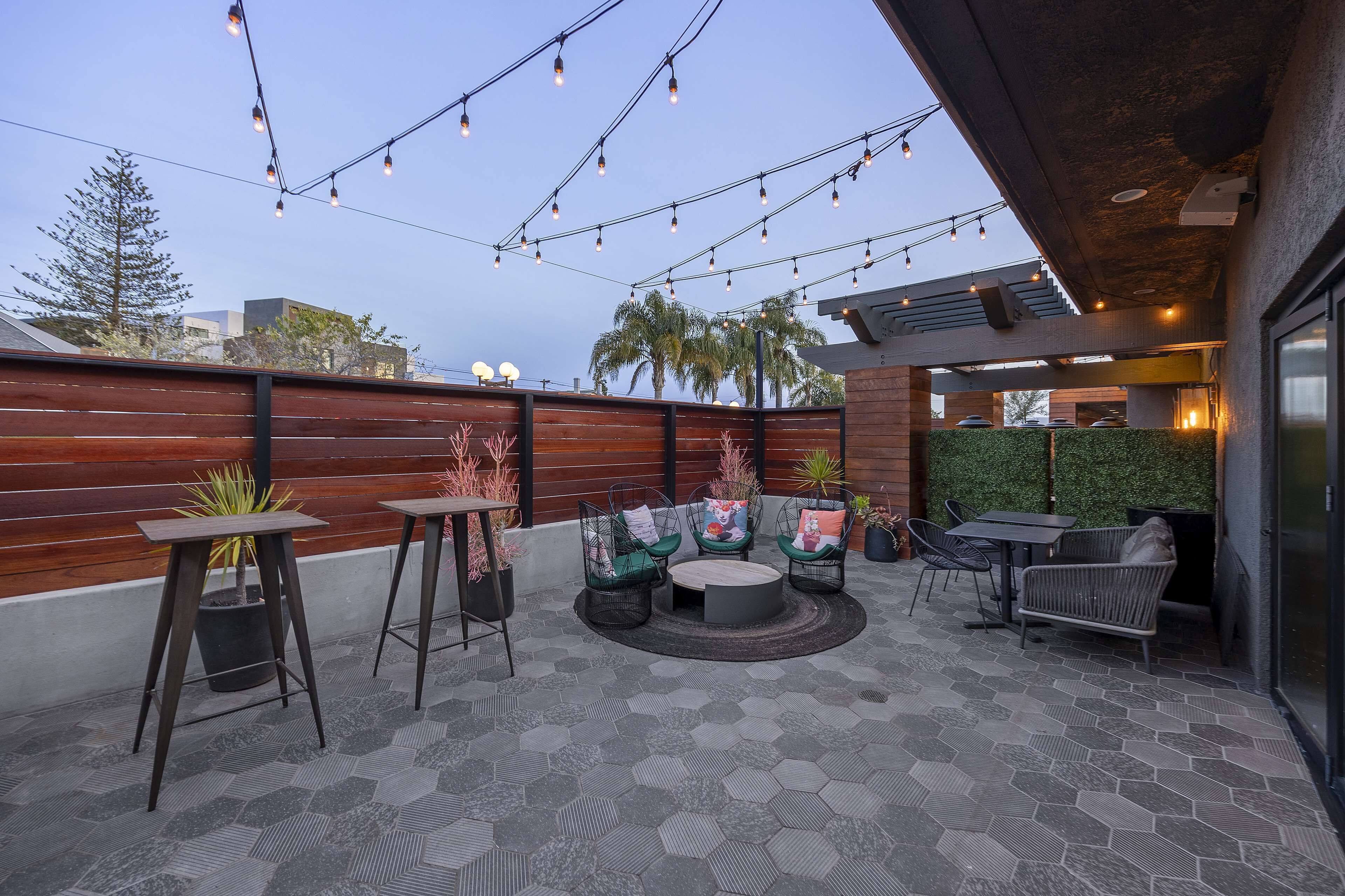 An outdoor patio with hexagonal tiles, wooden slatted walls, and string lights.