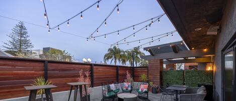 An outdoor patio with hexagonal tiles, wooden slatted walls, and string lights.