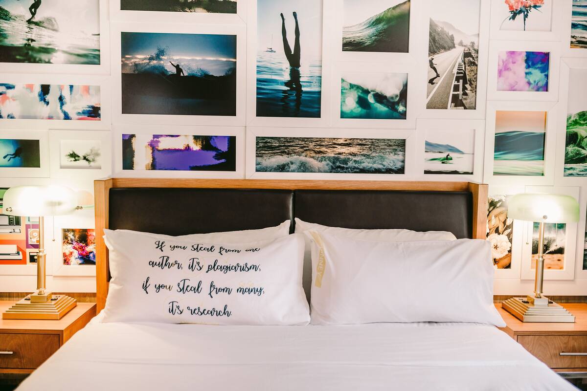 A hotel room with a bed, two nightstands, and a wall decorated with various photographs.