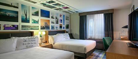 Una habitación de hotel con dos camas, un escritorio y un ventanal grande con cortinas.