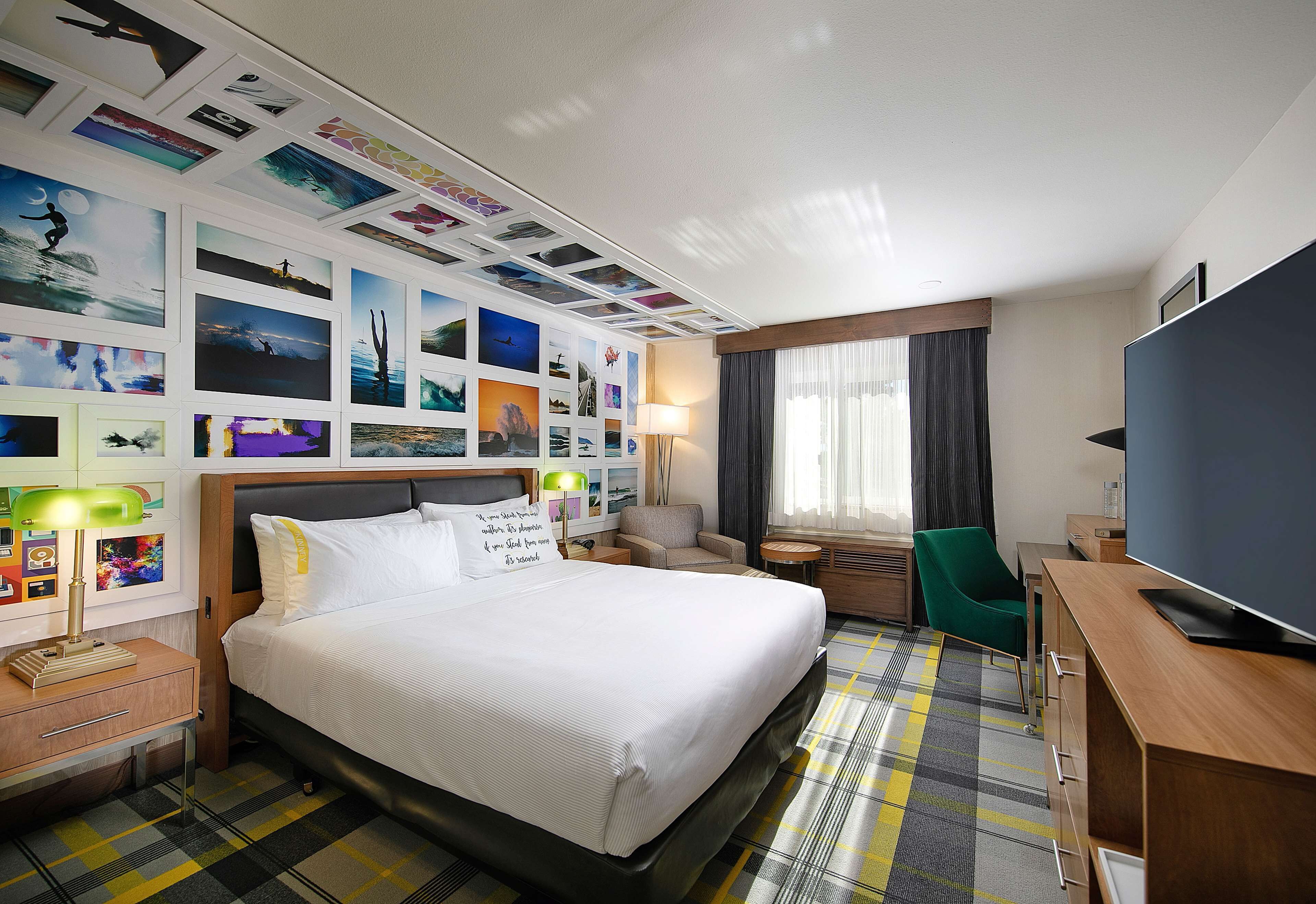 Camera d'albergo con un letto grande, una scrivania con televisione a schermo piatto, una sedia, una lampada e una parete decorata con diverse fotografie.