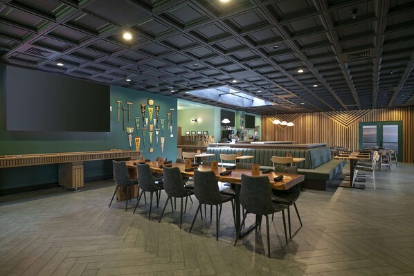 A modern restaurant with a high ceiling, wooden flooring, and a variety of seating options including tables and booths.