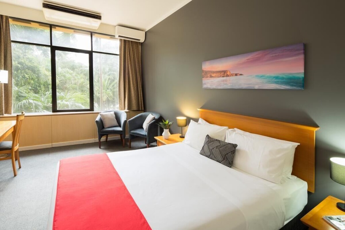 A hotel room with a large bed, a desk, a chair, and a window with curtains.