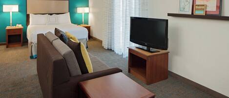A hotel room with a bed, a sofa, a TV on a stand, and a small table.