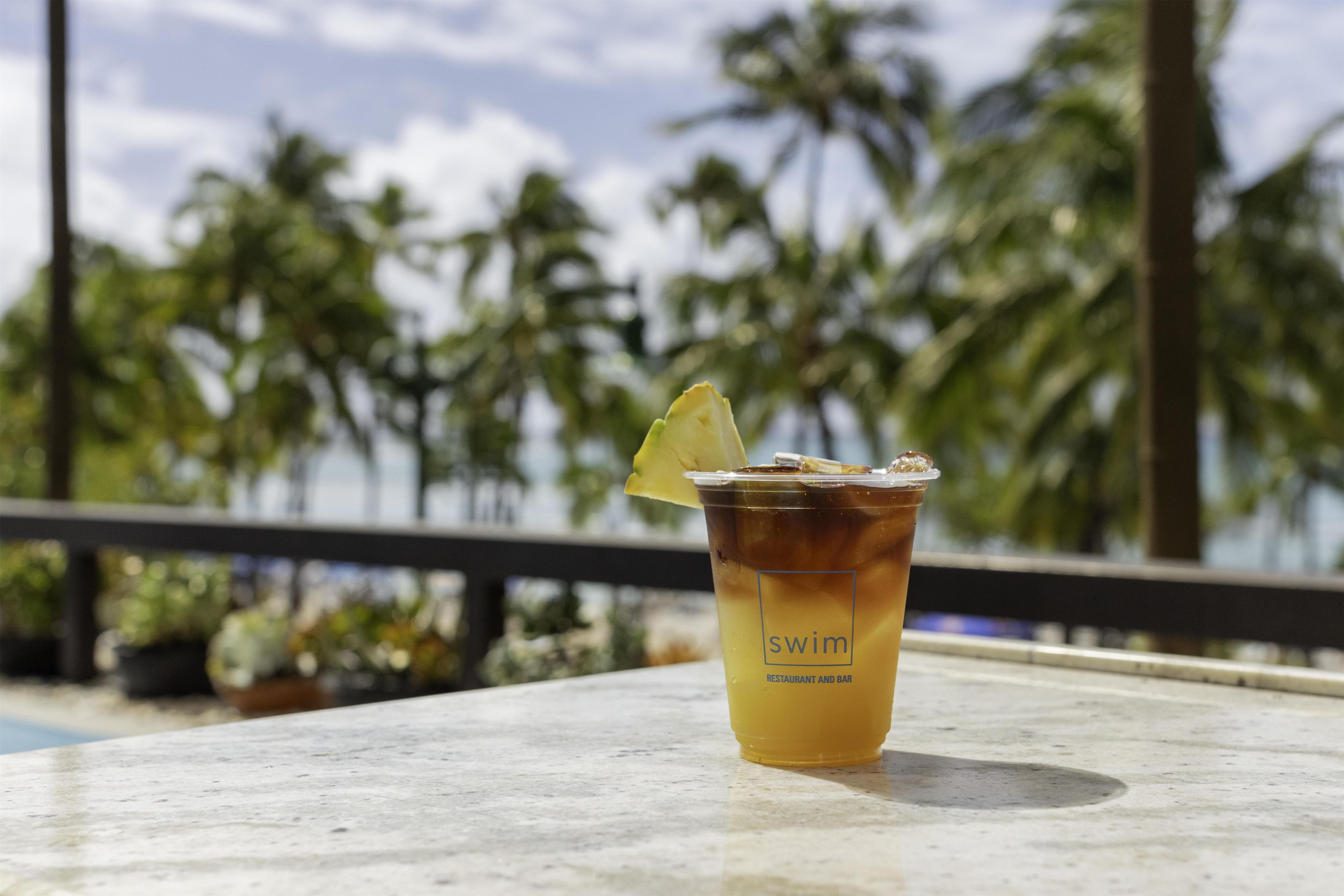A drink with a slice of lemon on a table with a view of palm trees.