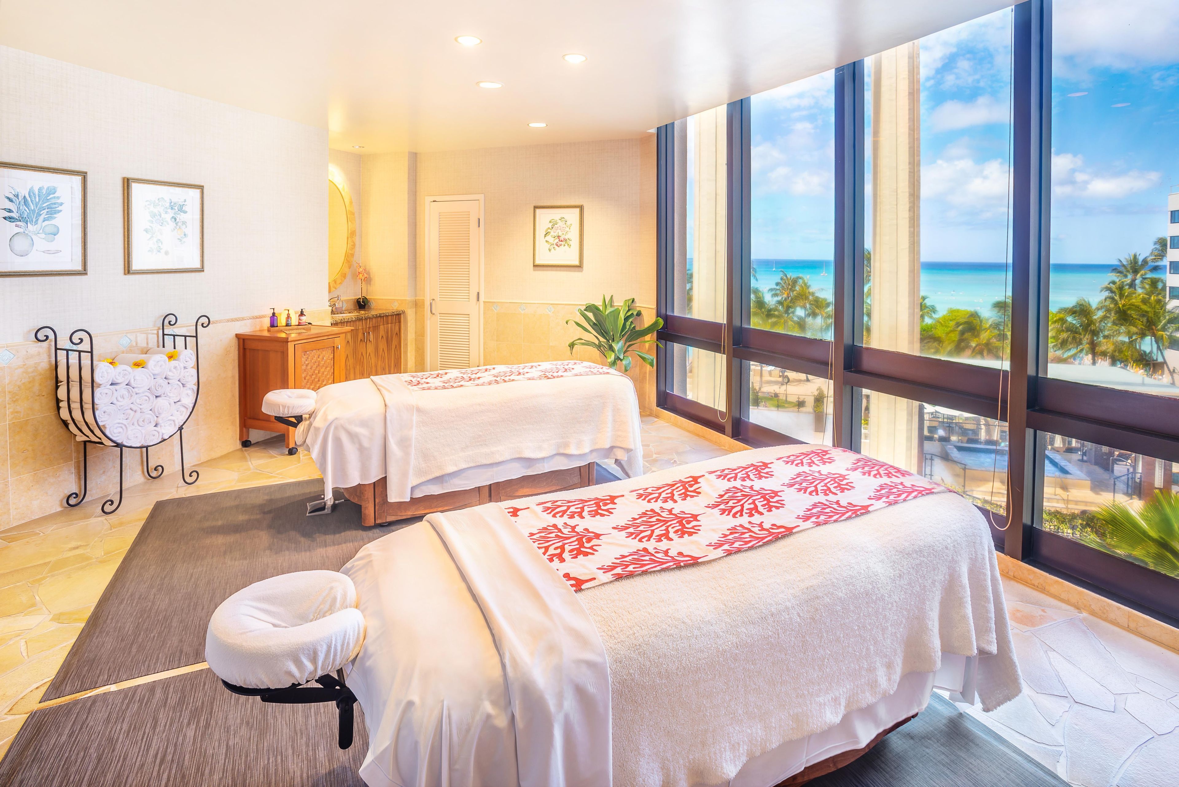 Un cuarto de spa con dos camas, una silla de masaje, tocador y un ventanal con vista a la playa.
