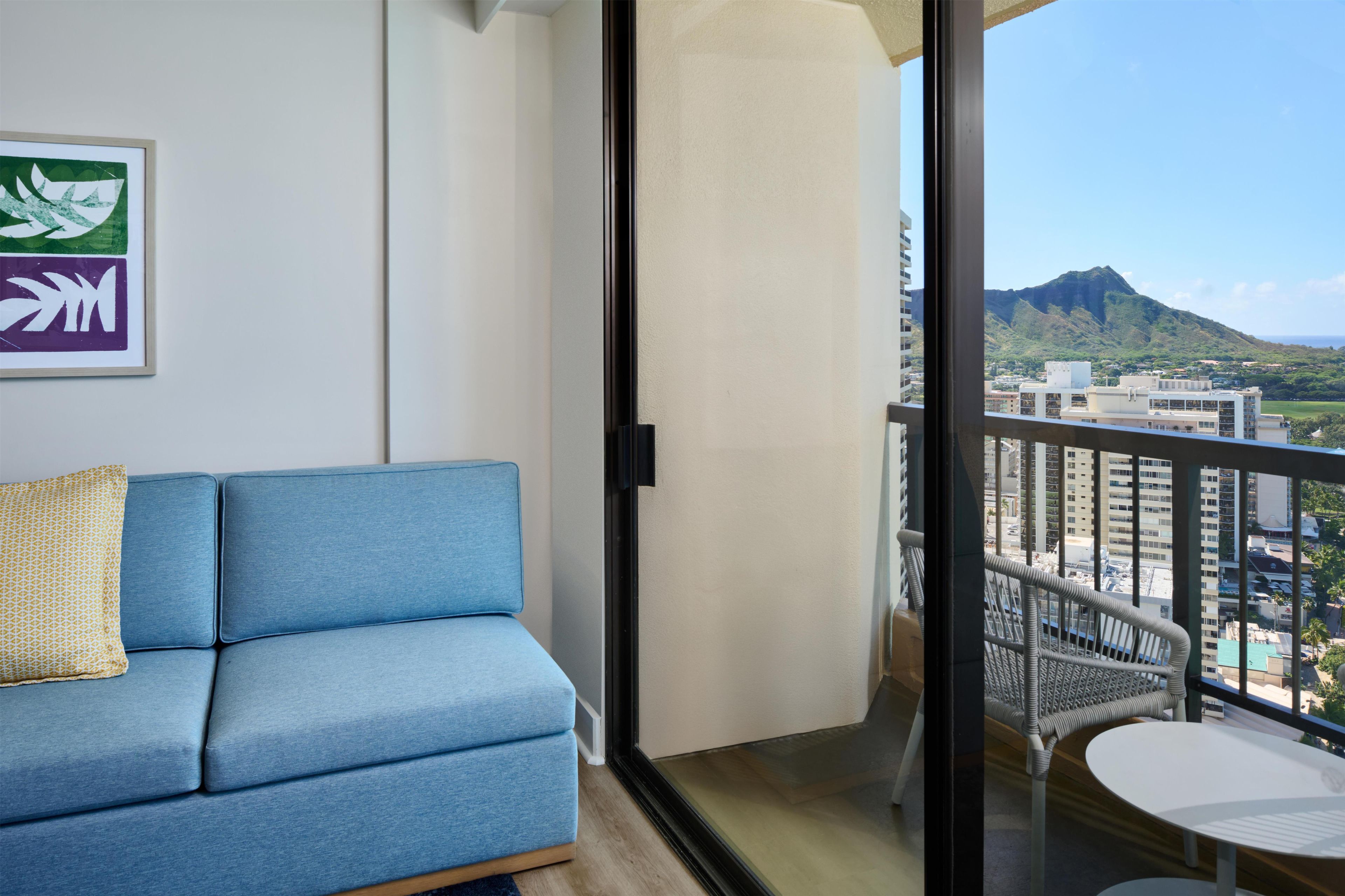 A balcony with a view of a mountain and cityscape, a blue sofa, and a small table.