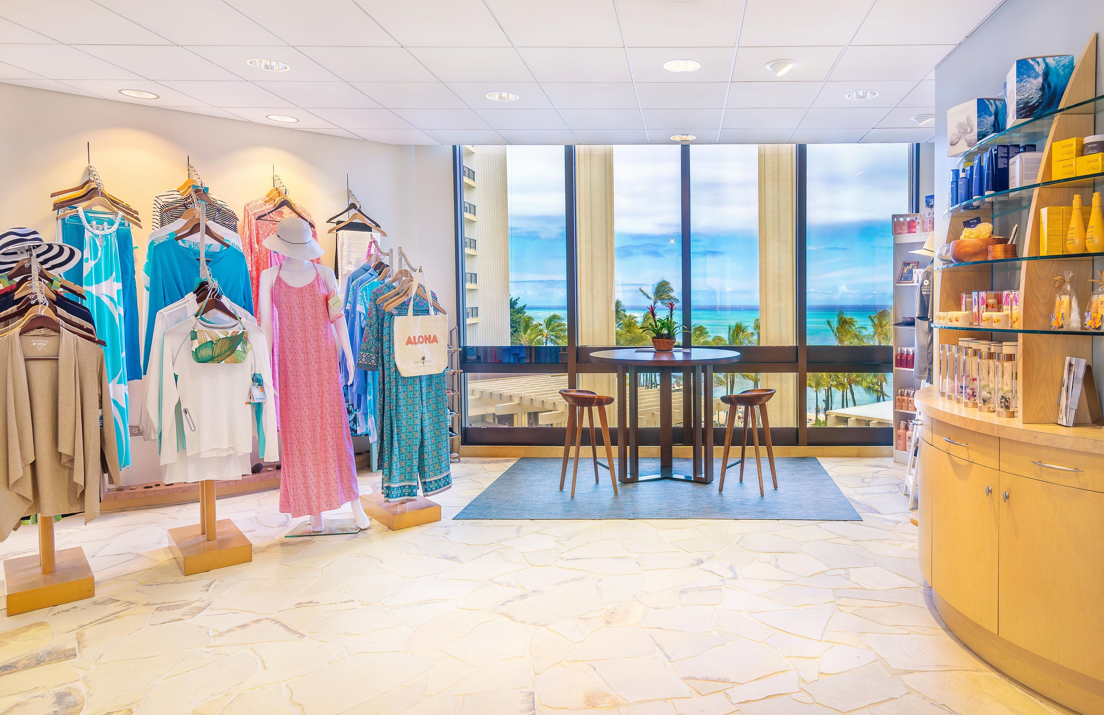 A clothing store with racks of dresses, a mannequin, and a view of the ocean through large windows.