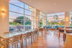A spacious indoor dining area with large windows, wooden flooring, and modern furniture.