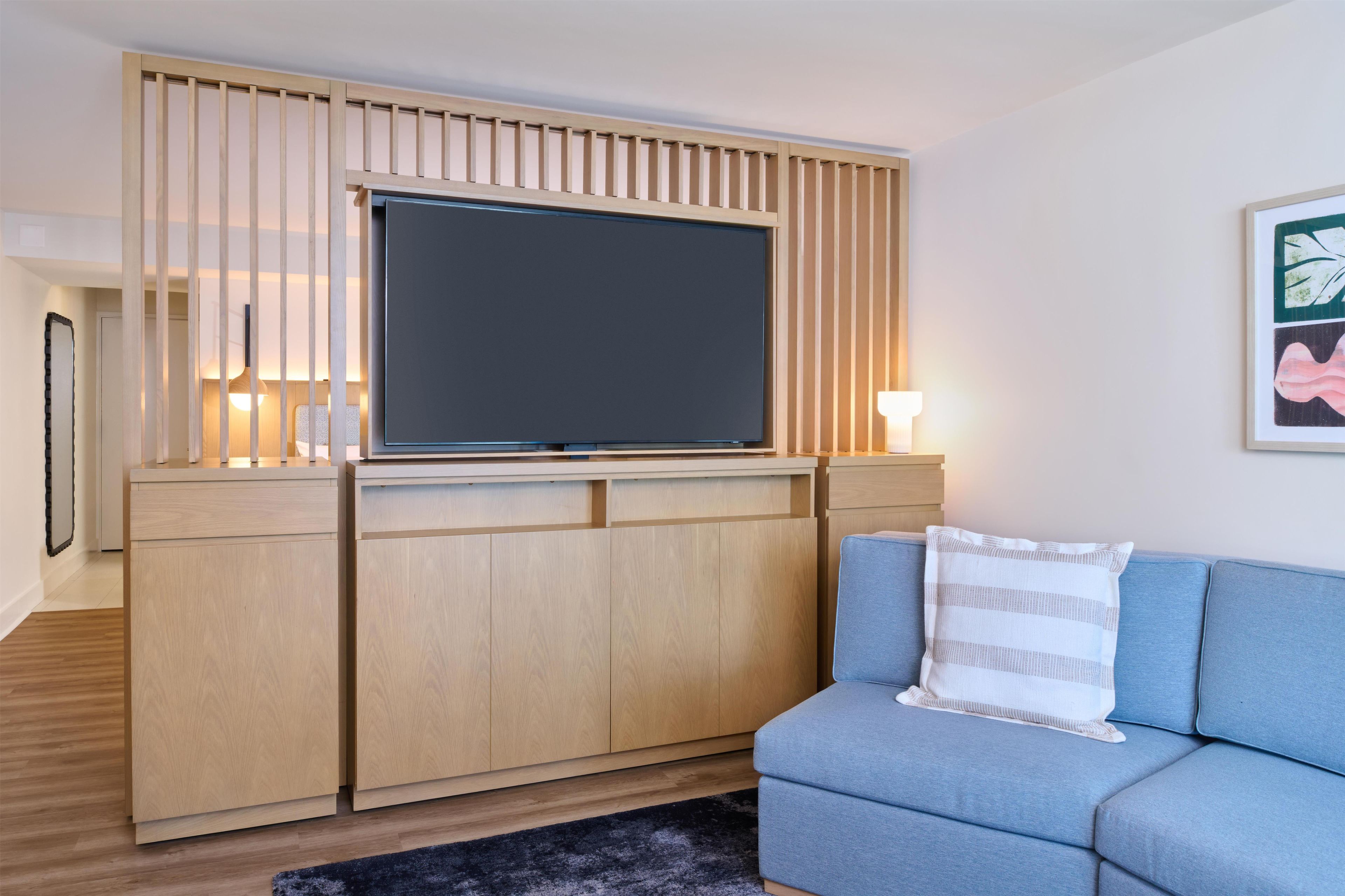 Ein modernes Wohnzimmer mit einem Flachbildfernseher auf einem Holzboden, einem blauen Sofa und einem schwarzen Teppich.