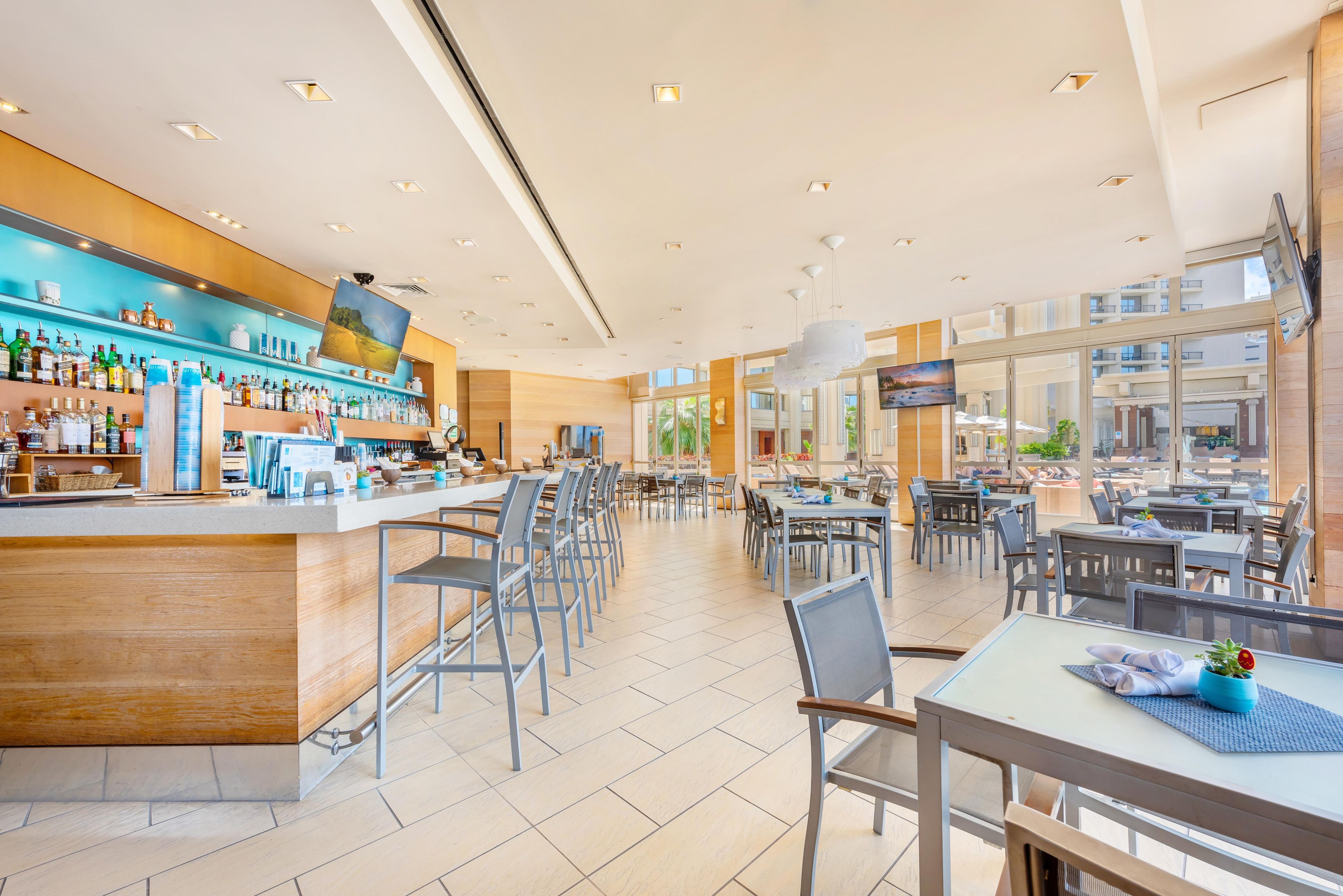 A modern bar area with a counter, seating, and a TV screen.