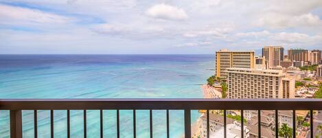 A balcony with wicker furniture overlooking a beach and cityscape.