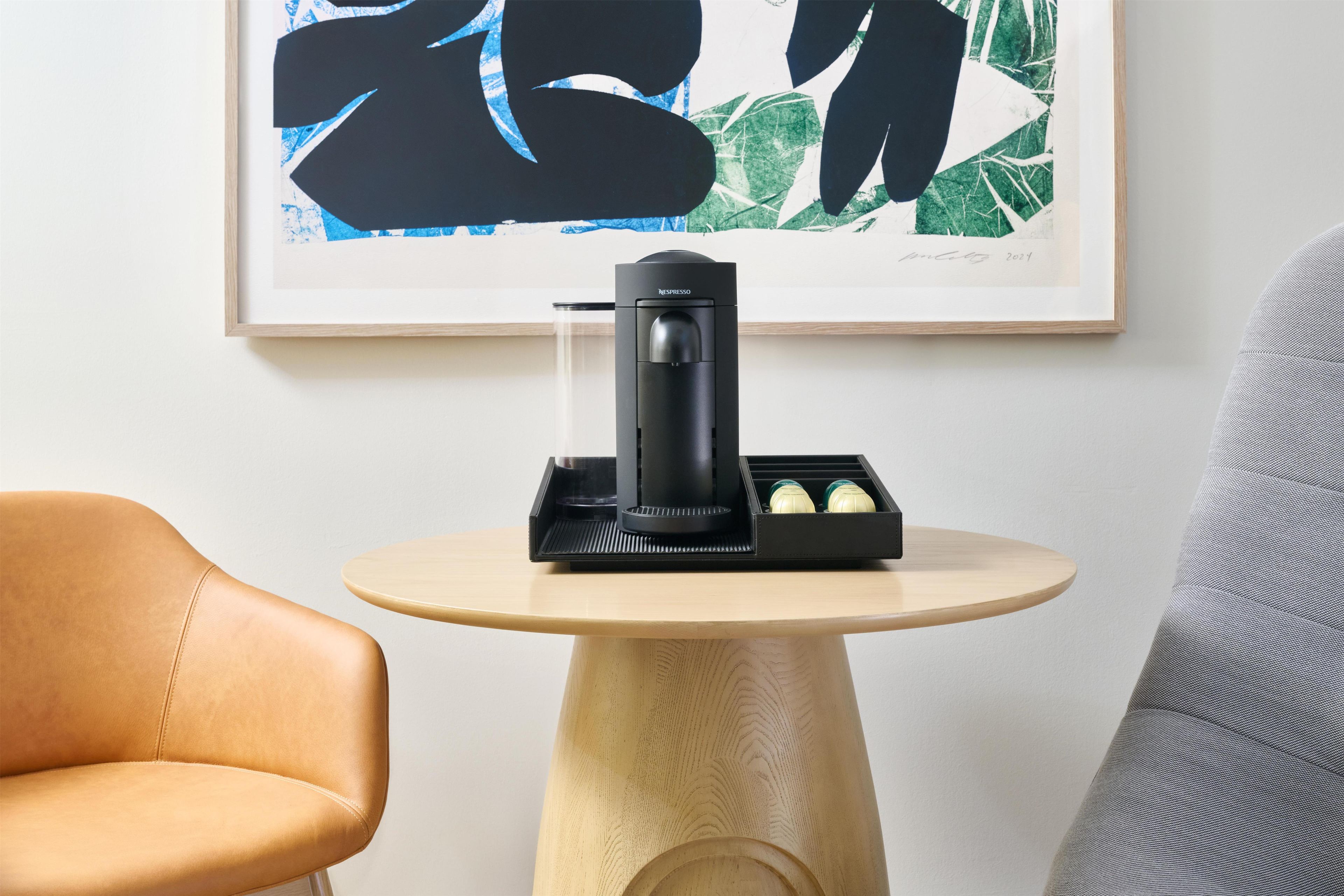 A modern coffee machine on a wooden table with a framed artwork above it.