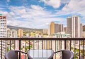 A balcony with wicker chairs and a city view.
