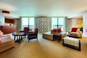 A spacious hotel room with a large window, a sofa, a chair, a small table, and a decorative wall.
