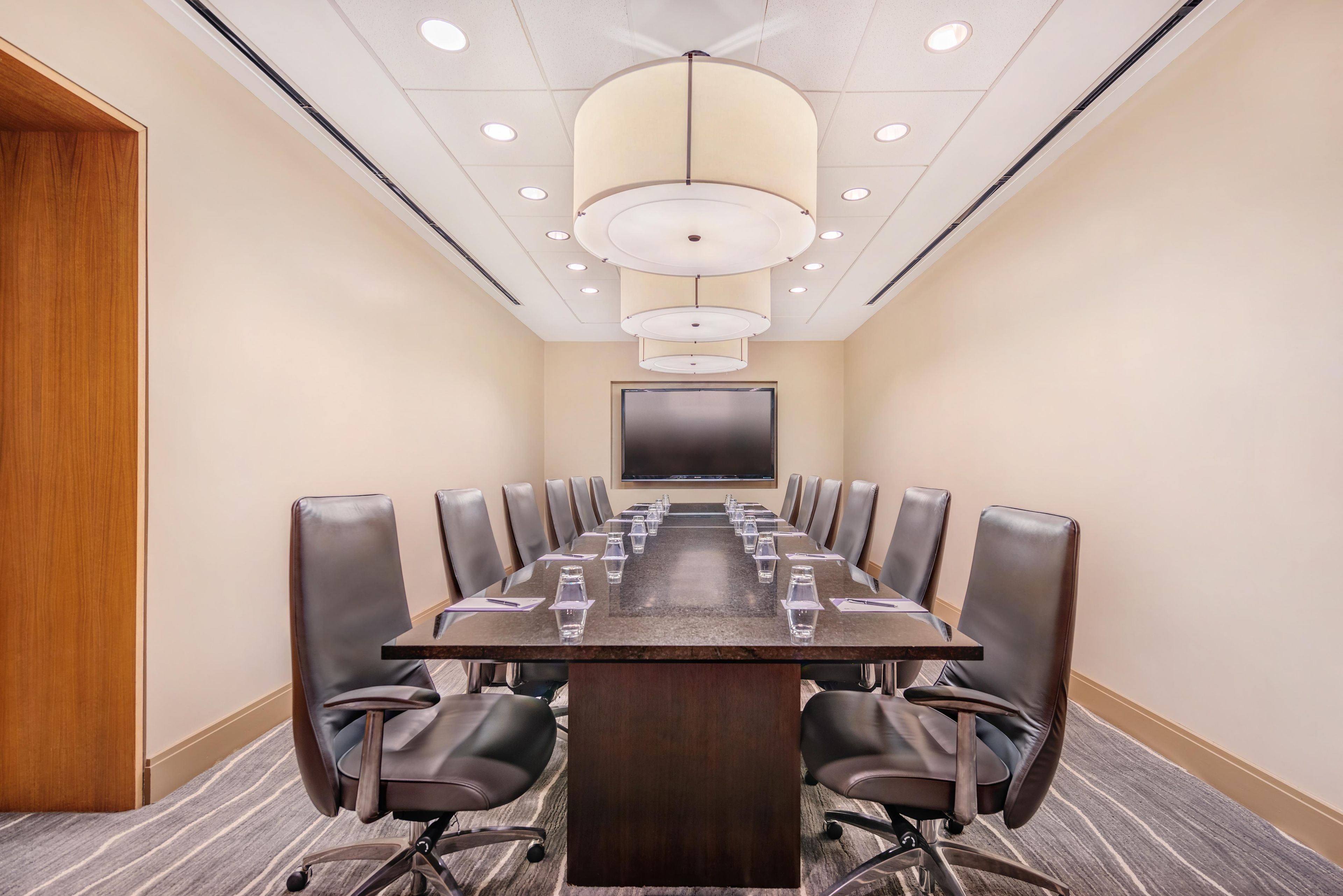 A conference room with a long table, chairs, and a large screen at the front.