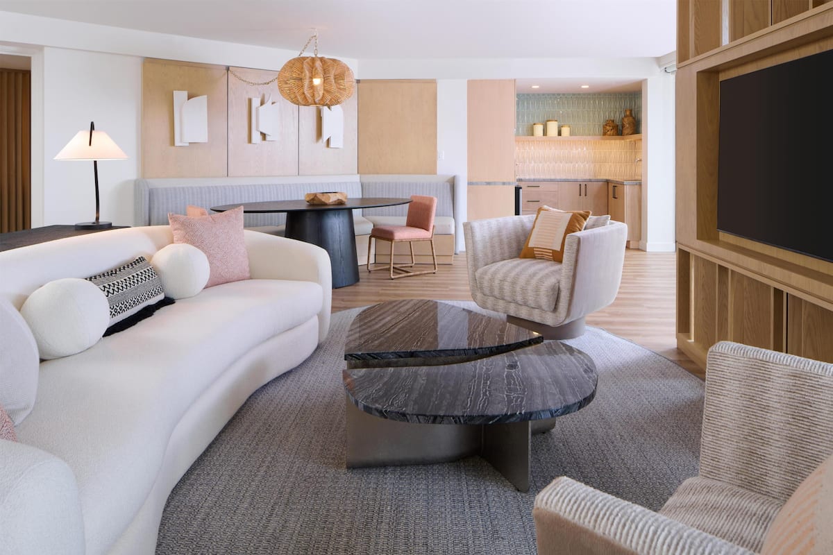 Ein modernes Wohnzimmer mit Sofa, Sessel und Couchtisch, ein Essbereich mit Tisch und Stühlen sowie eine Küche mit Holzausstattung und Arbeitsplatte.