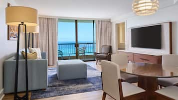 A modern hotel room with a balcony, a flat-screen TV, a glass dining table, and a sofa.