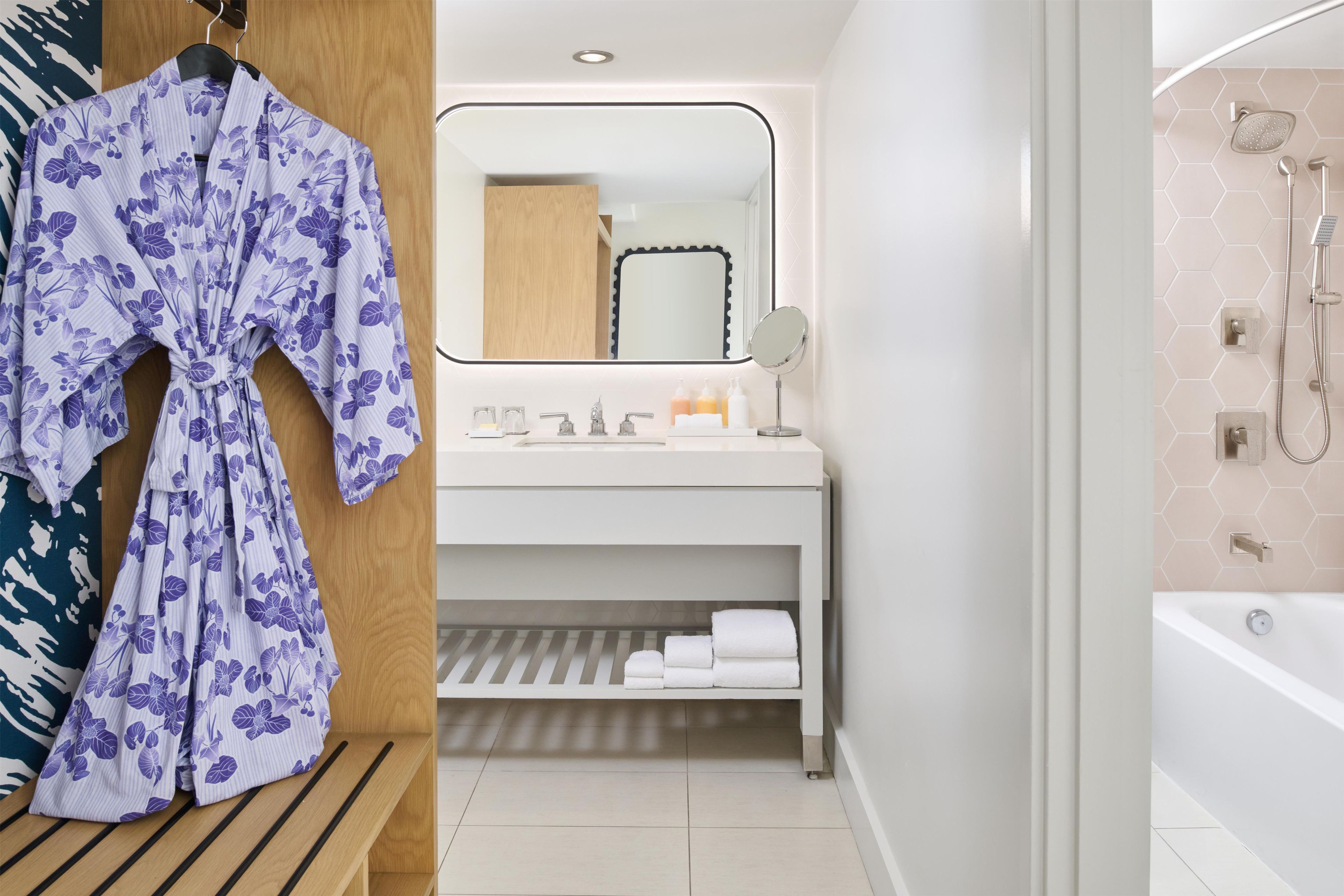 A bathroom with a shower, a sink with a mirror, and a bench with towels.
