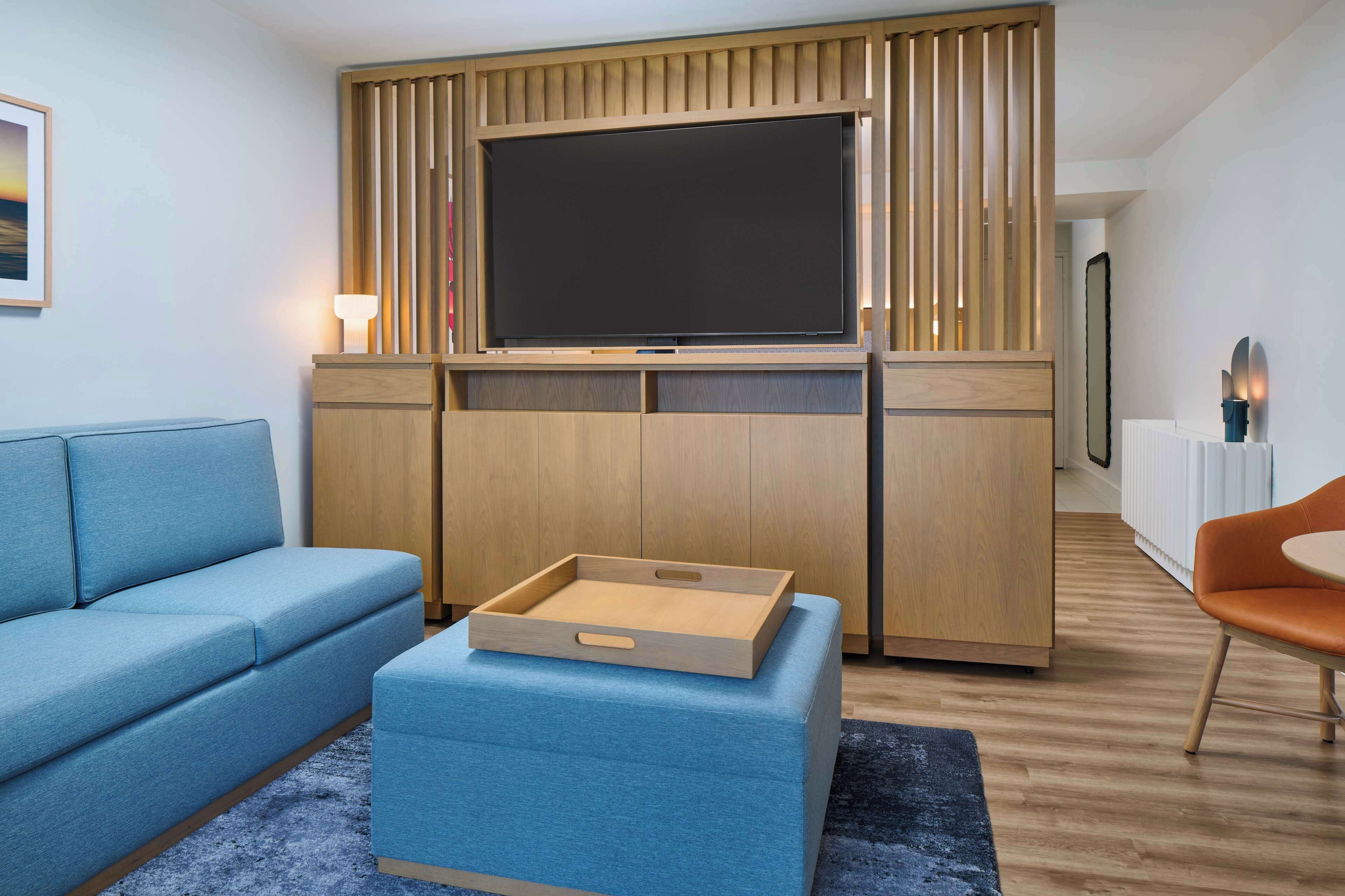 Un salon moderne avec un téléviseur à écran plat, un canapé bleu, un meuble de rangement en bois et un petit fauteuil orange.