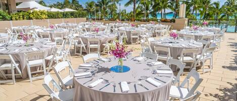 Outdoor round tables with white chairs, arranged in rows, set up for dining.