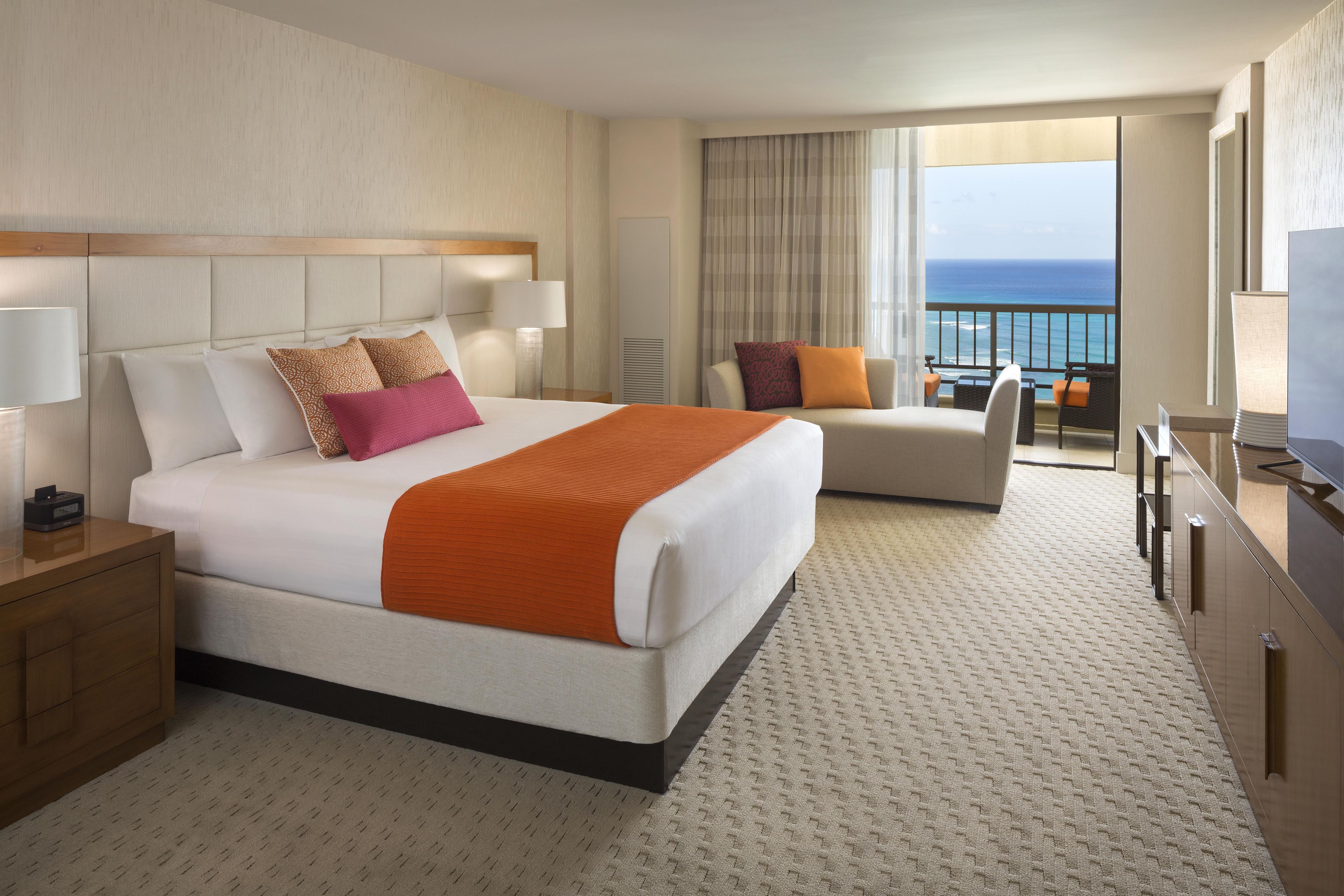 Habitación de hotel con cama, una silla, un escritorio y vista al océano.