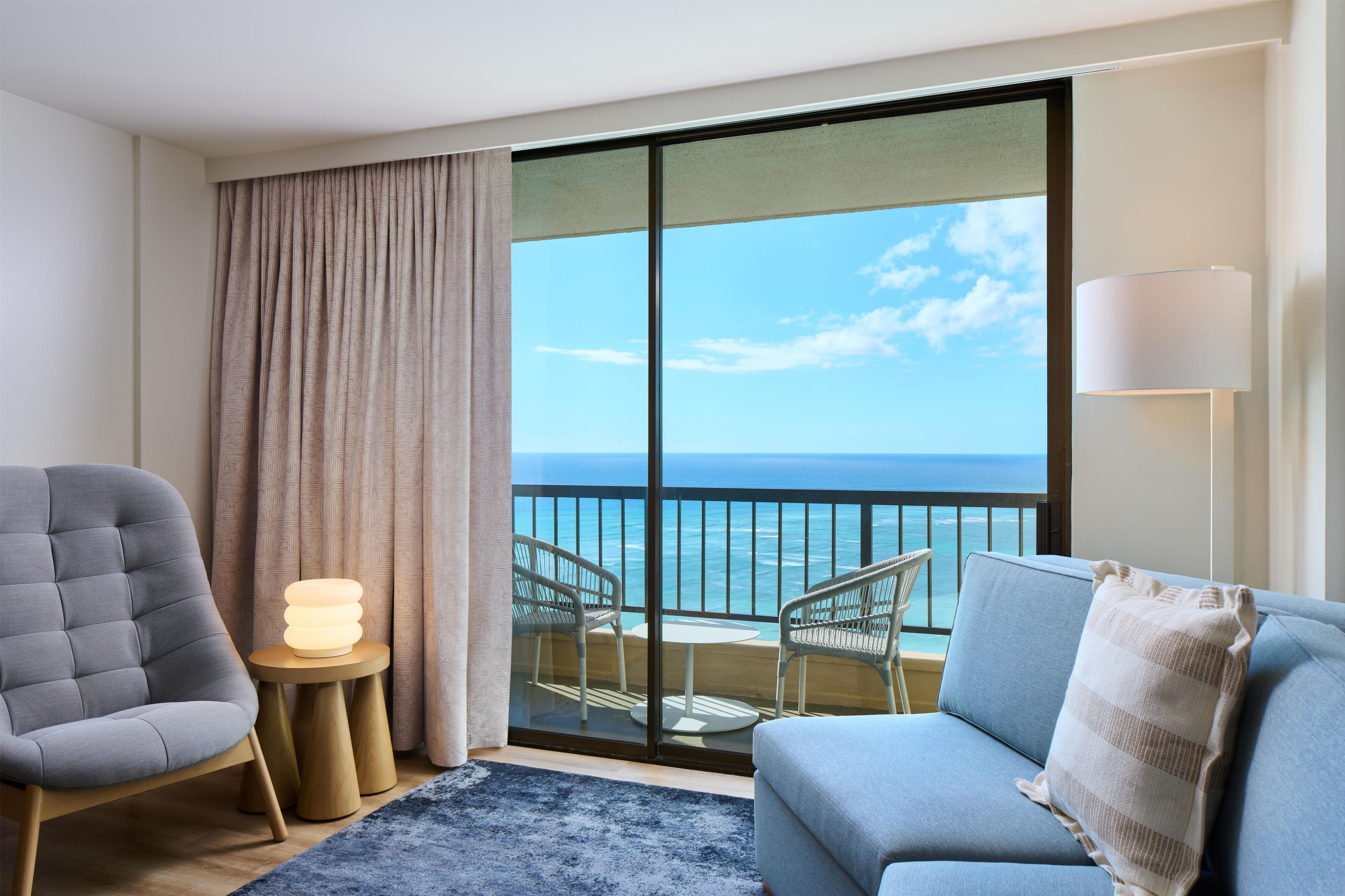 Une chambre d’hôtel avec un balcon, un canapé, un fauteuil, une lampe et une table d’appoint.