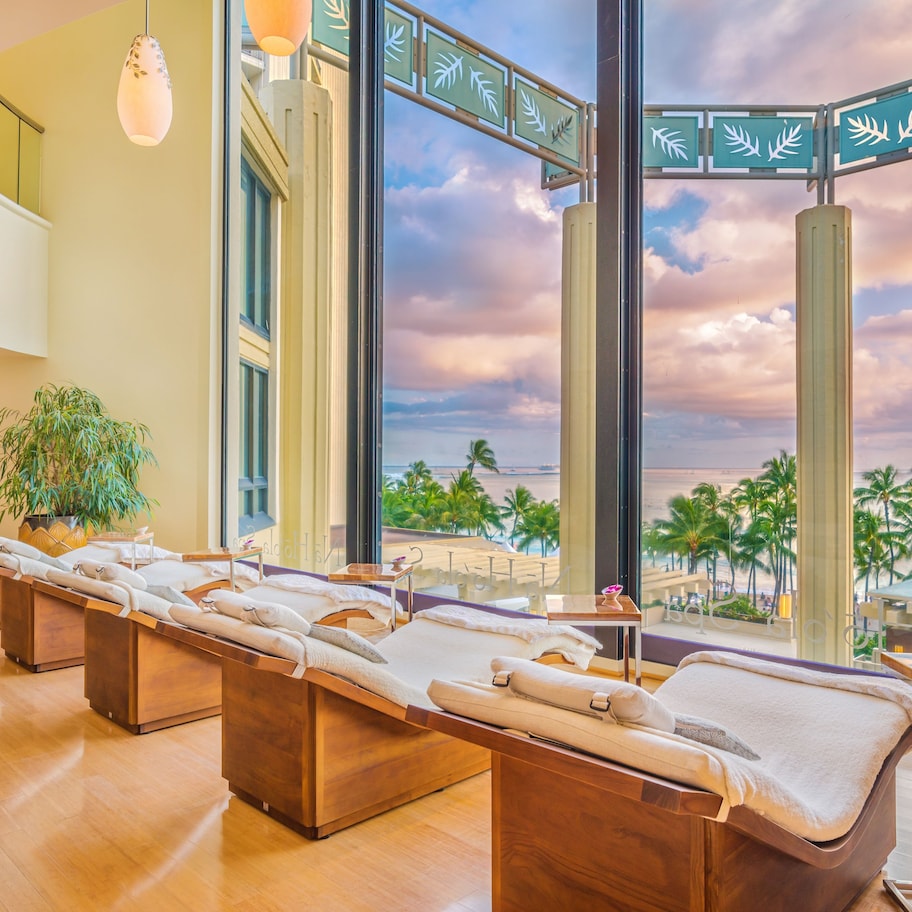 A spa room with two massage tables, a large potted plant, and a view of the beach.