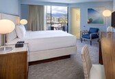 A hotel room with a large bed, a desk, a chair, and a view of the cityscape.