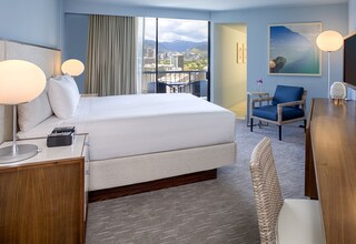 A hotel room with a large bed, a desk, a chair, and a view of the cityscape.