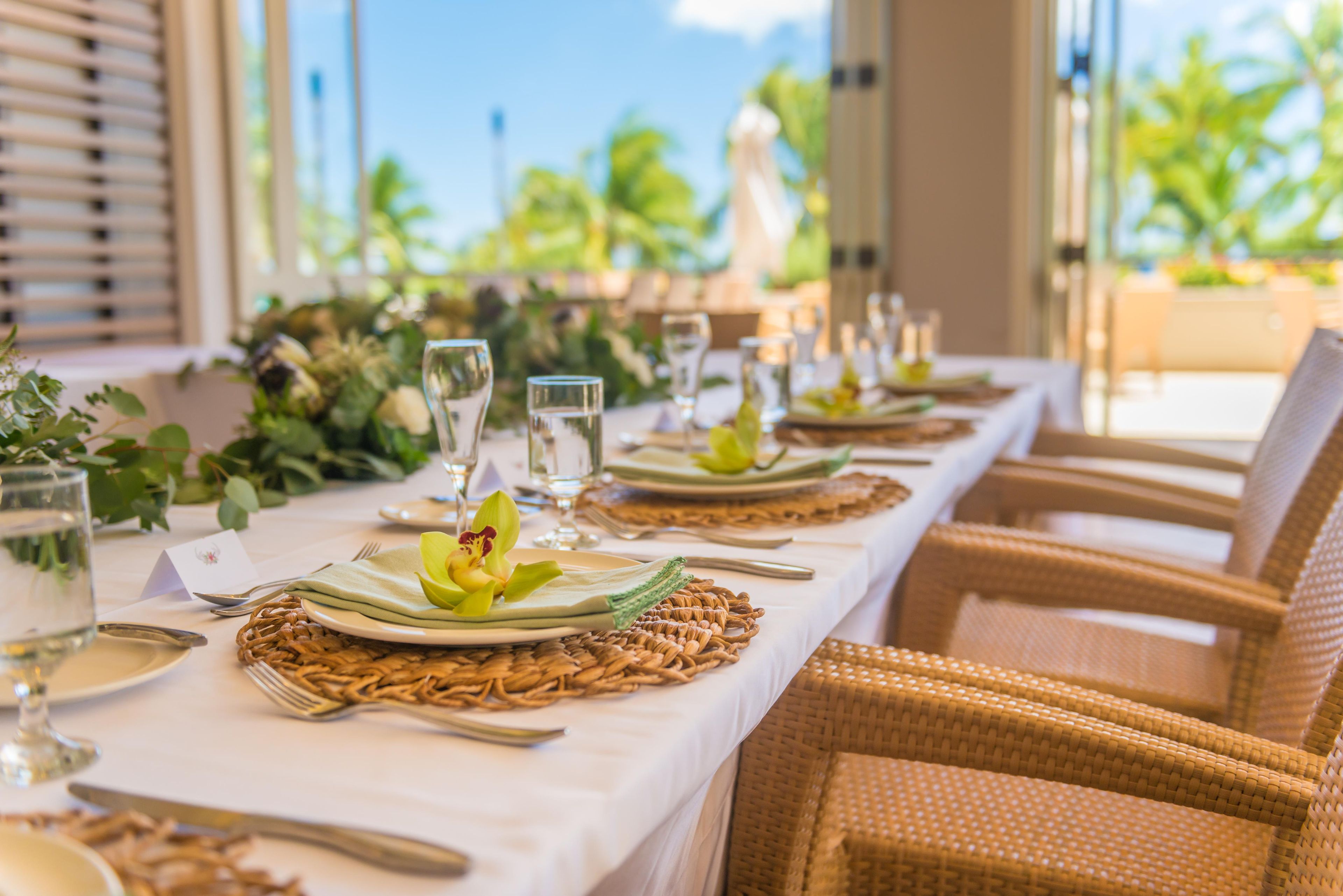 A dining table set with plates, cutlery, and glasses, surrounded by wicker chairs.
