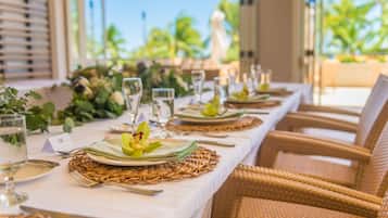 A dining table set with plates, cutlery, and glasses, surrounded by wicker chairs.