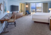 A hotel room with a bed, desk, chair, TV, and a view of the ocean.