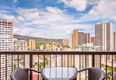 A balcony with wicker chairs, overlooking a cityscape with high-rise buildings and a distant mountain.