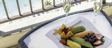 Ein Tisch mit einer Obstplatte und zwei Gläsern Weißwein auf einem Balkon mit Blick auf einen Strand.