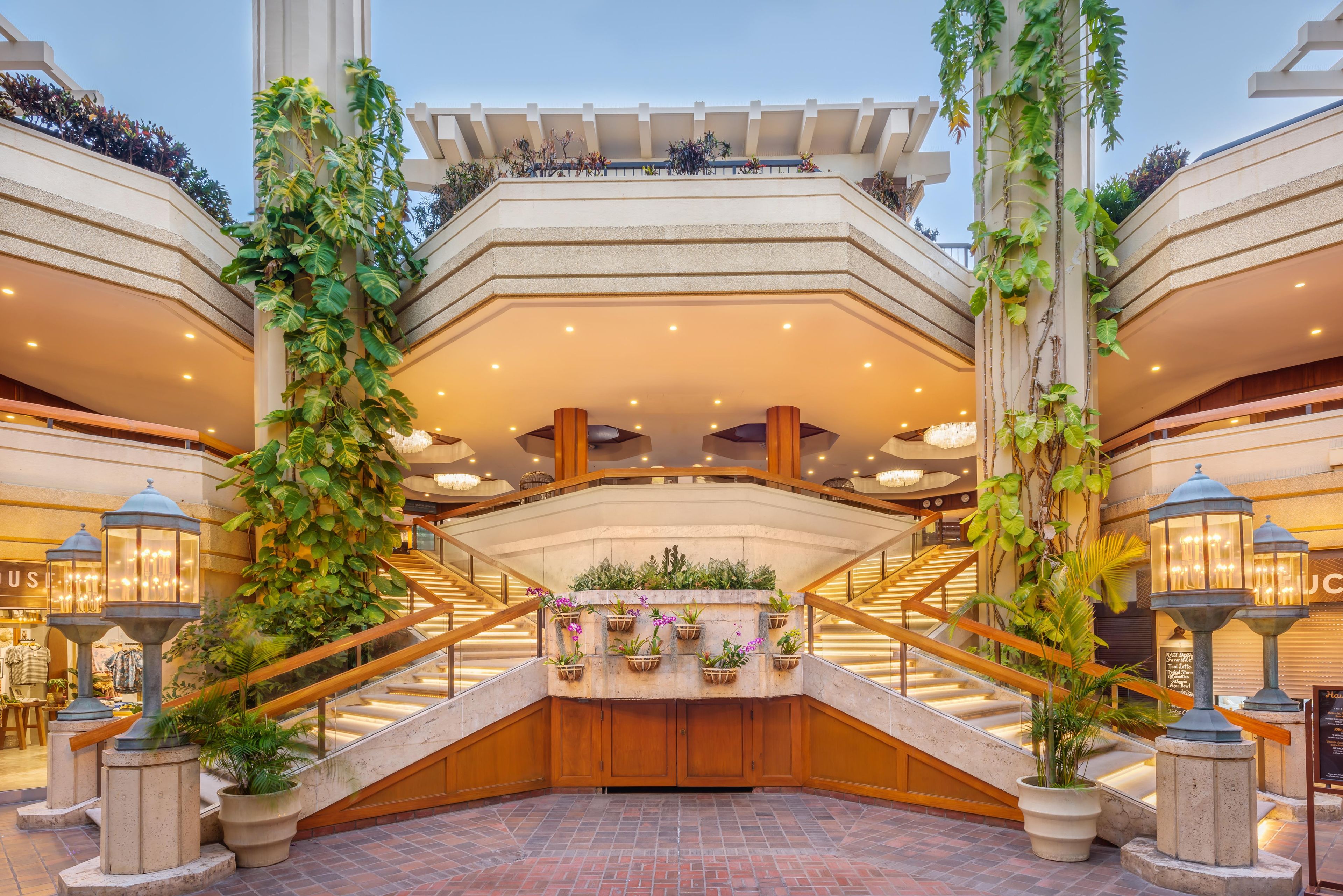 Un vestíbulo de hotel con una escalera central, plantas en macetas e iluminación empotrada en el techo.