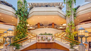 A hotel atrium with a central staircase, potted plants, and a ceiling with recessed lighting.
