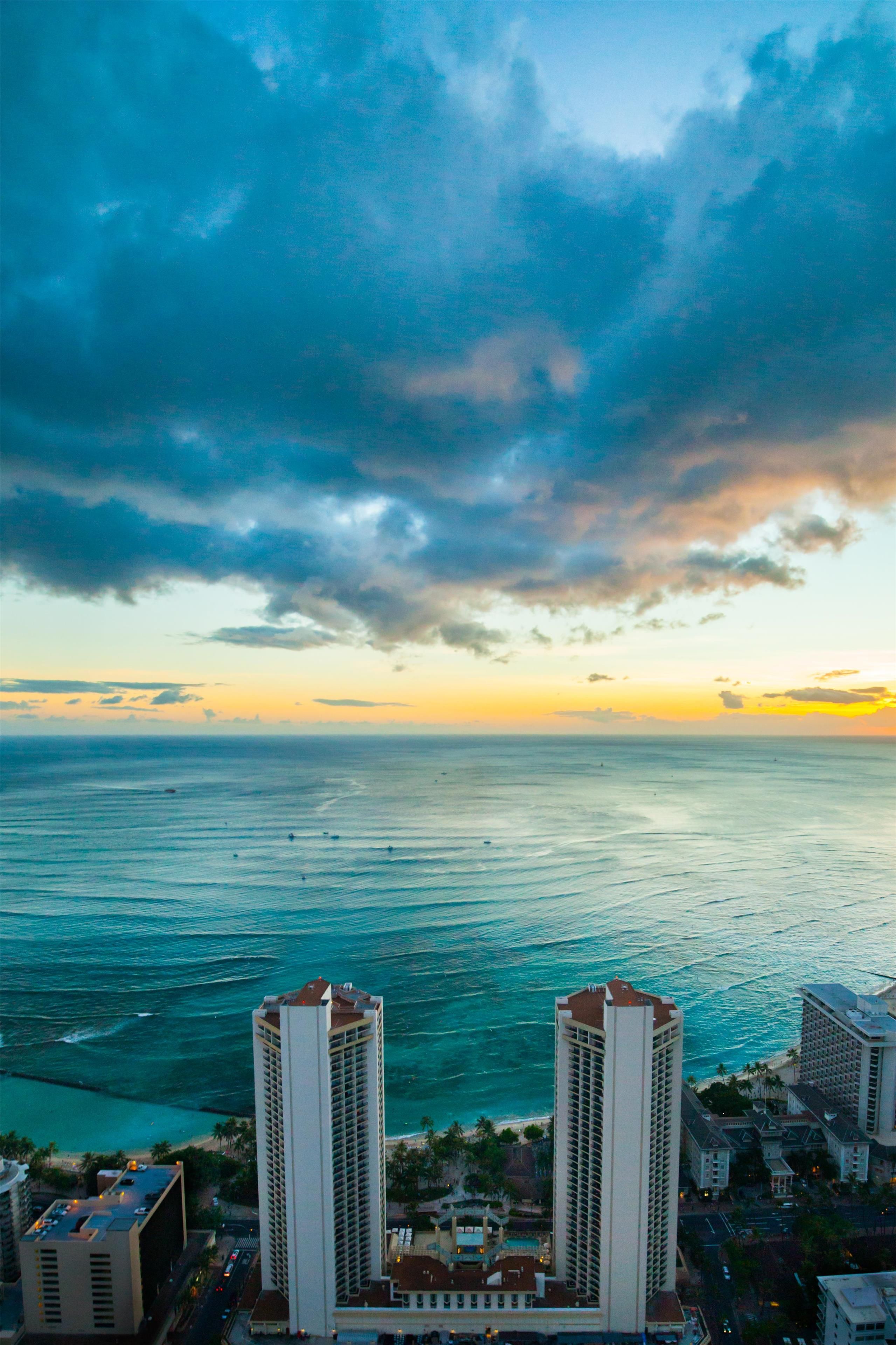 A coastal cityscape with high-rise buildings, a view of the ocean, and a sunset sky.