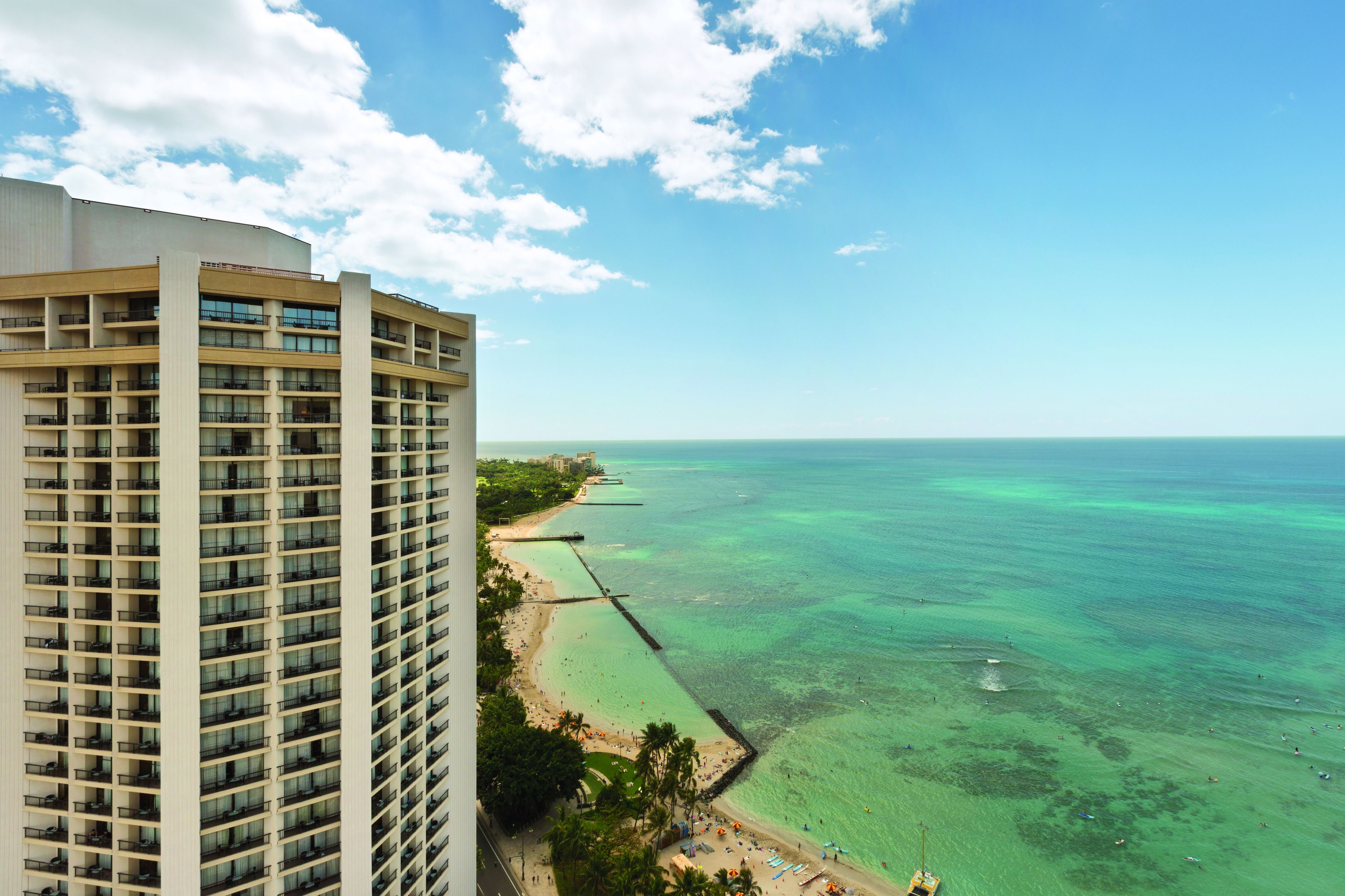 A high-rise hotel overlooking a beach with clear turquoise waters and a pier extending into the sea.