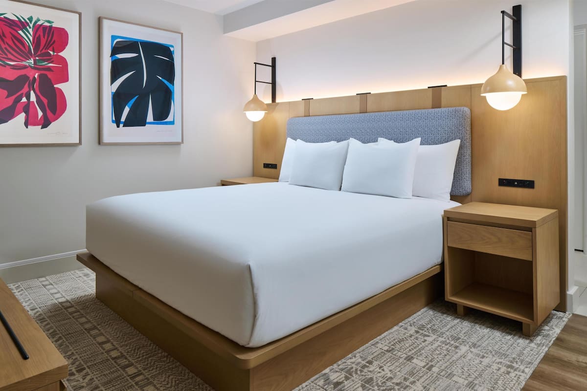 A modern hotel room with a large bed, wooden headboard, two bedside tables, and two wall-mounted lamps.
