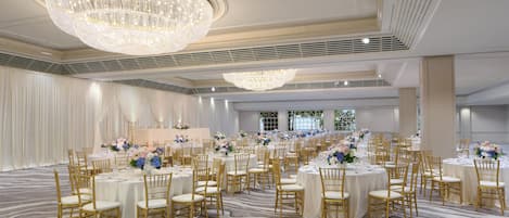 A banquet hall with round tables, gold chairs, and a large chandelier.