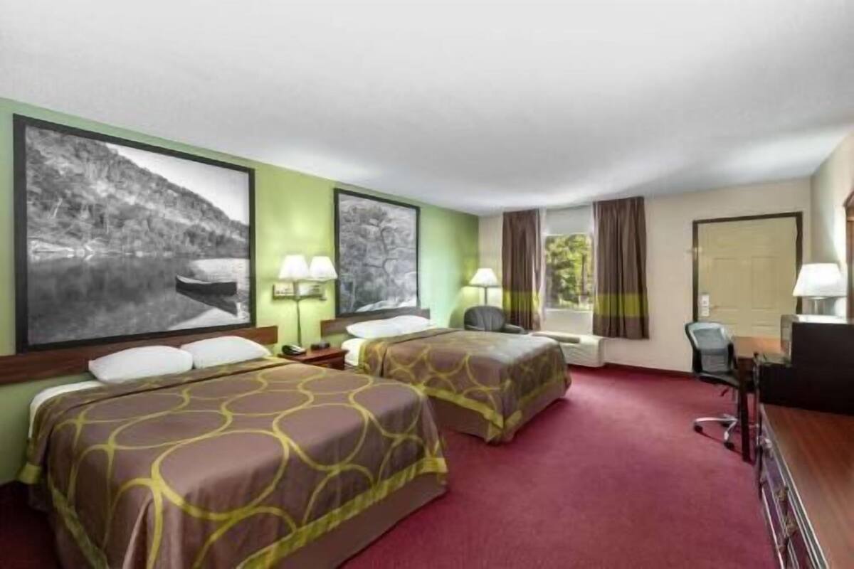 Una habitación de hotel con dos camas, un escritorio, una silla y un ventanal con cortinas.